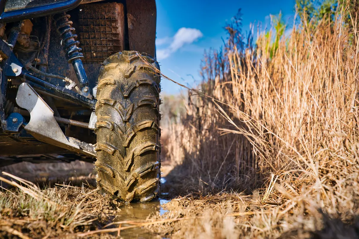 Close-up of a muddy side-by-side tire and front suspension sitting in water on a wet trail