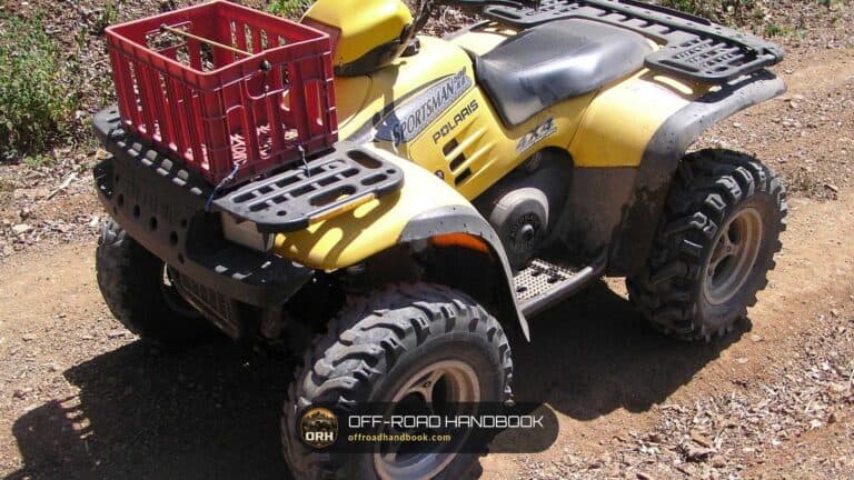 Yellow ATV with a straddle seat and a red crate on the rear rack, parked on a dirt trail