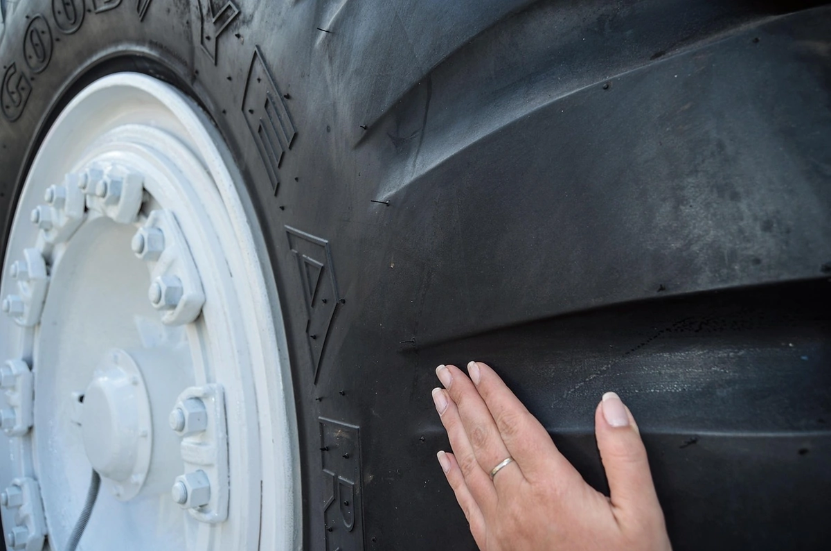 Hand resting on the sidewall of a large tire with a white wheel to show its size