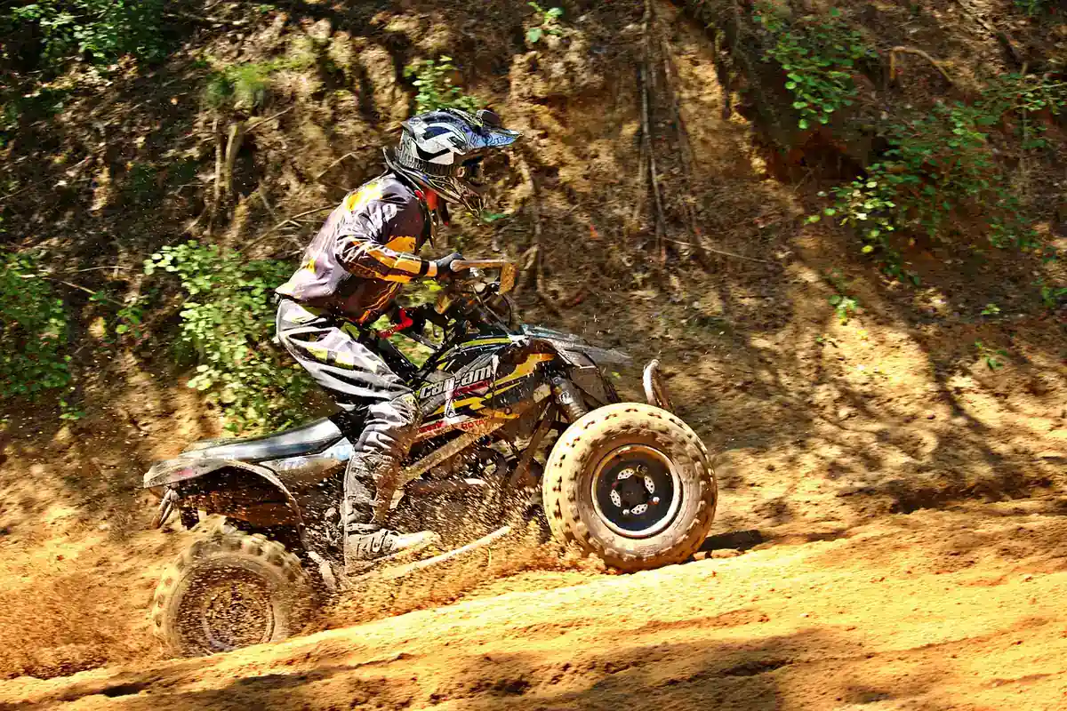Sport quad rider in a full-face helmet leaning into a dirt corner beside a dirt bank