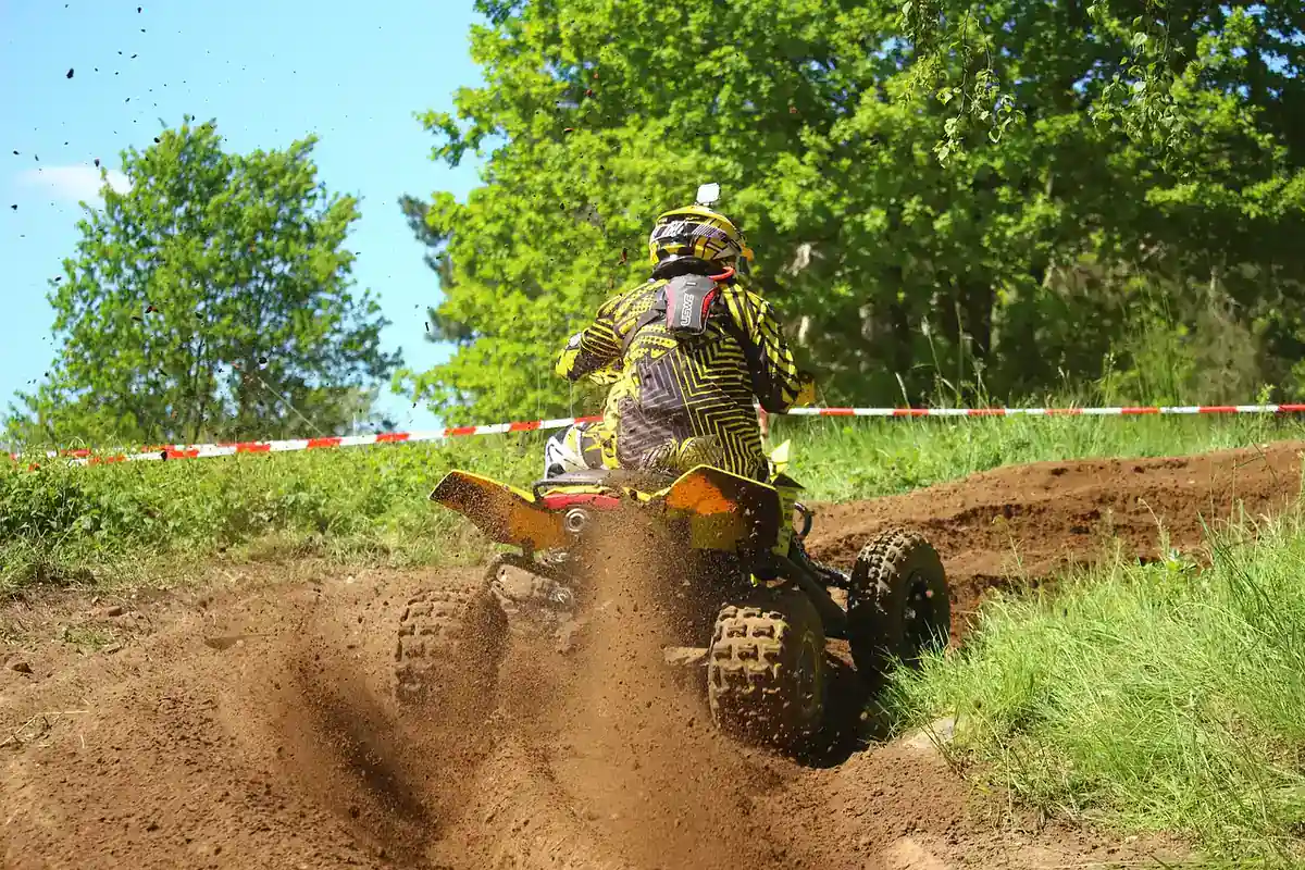 Rider in yellow gear on a sport quad throwing dirt on a grassy motocross track