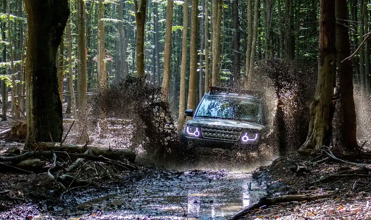 SUV driving through a muddy forest track with mud and water thrown up around it
