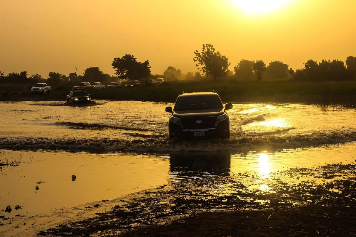 SUV driving through shallow standing water on a dirt track at sunrise