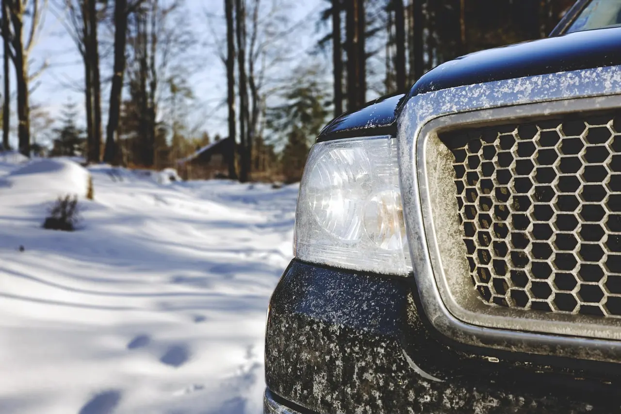 Front grille and headlight of a dark SUV beside a snow-covered path in the woods