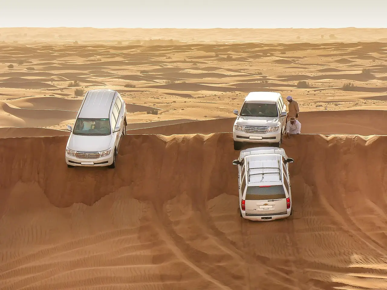 Three SUVs stopped on a sand dune ridge in a hot desert
