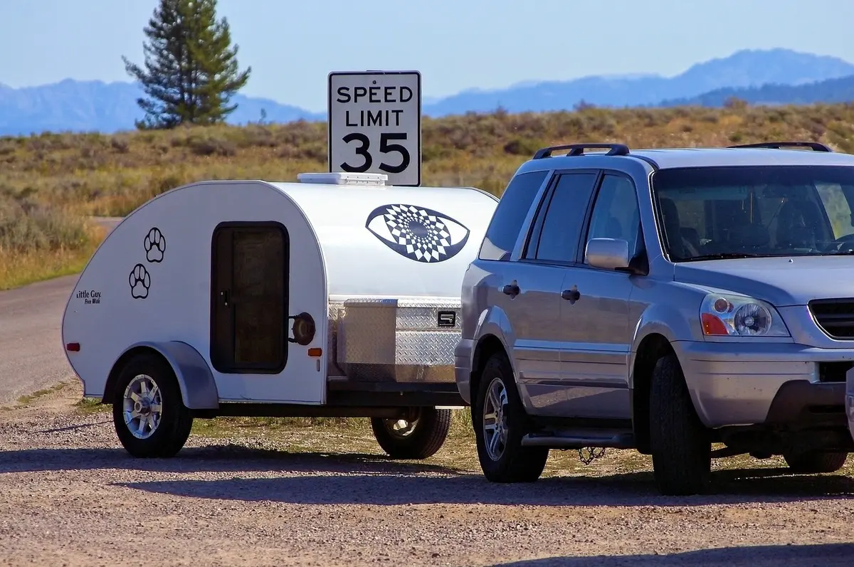Small teardrop camper trailer hitched to a midsize SUV parked beside a 35 mph speed limit sign