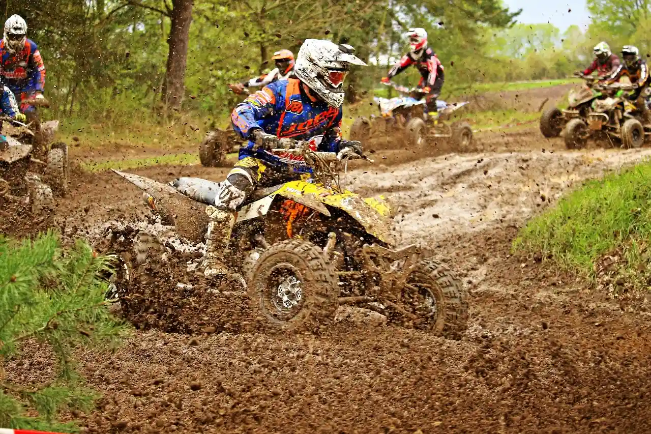 An ATV rider in a helmet leaning through a muddy corner on a wooded trail