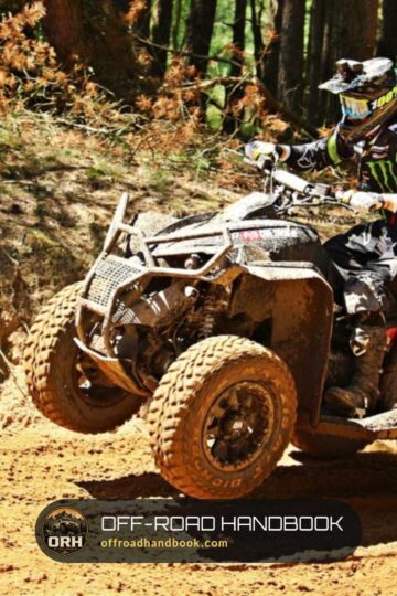 An ATV rider in a helmet crossing a muddy dirt bank beside a pine forest
