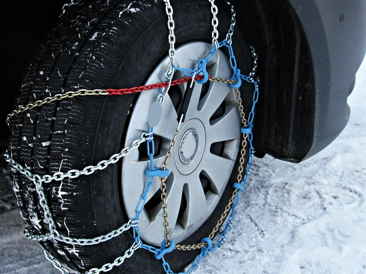 Link tire chain with blue tensioner installed over a car tire on packed snow