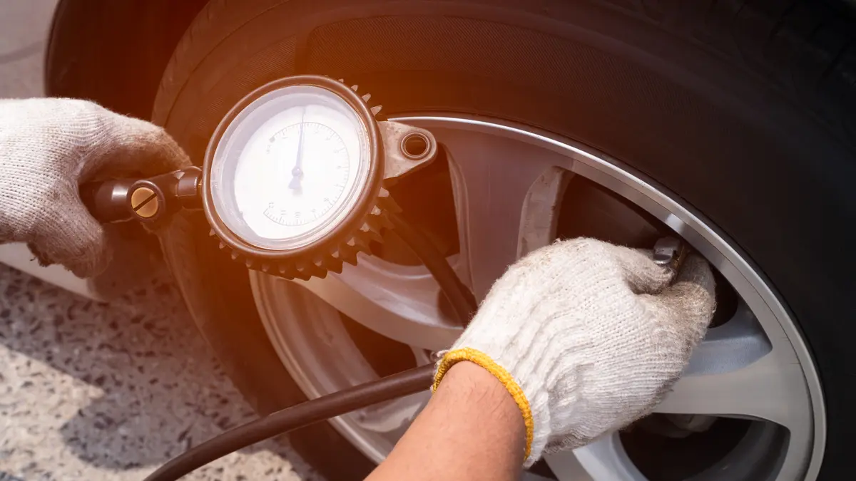 Gloved hands holding a dial tire pressure gauge on a wheel valve stem