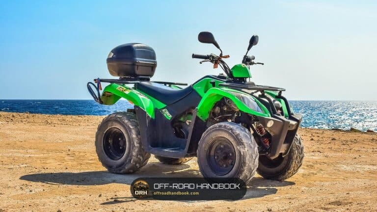 Green ATV with a rear cargo box parked on a sandy shore, stock photo of an ATV and not a Tracker 800SX