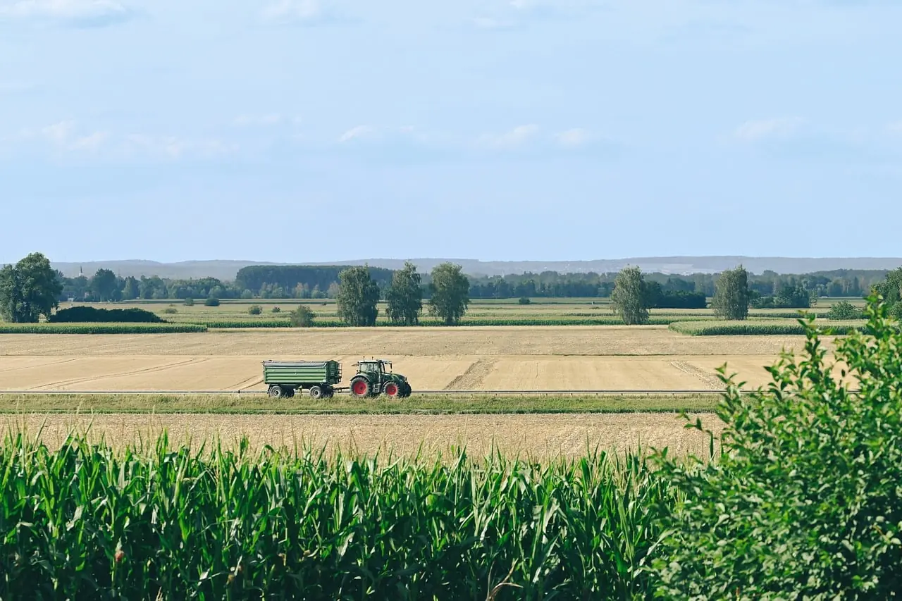 Tractor pulling a green trailer along a farm field under a blue sky