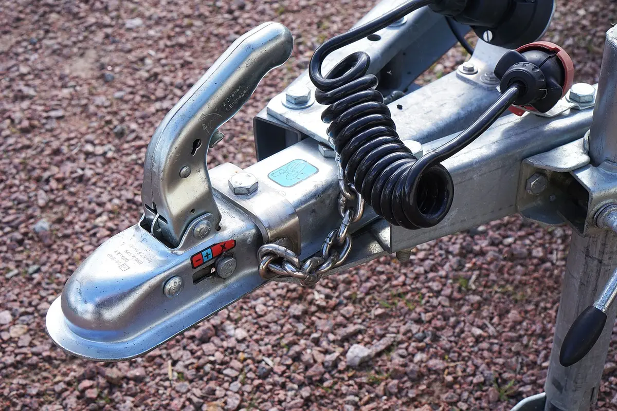 Close-up of a trailer coupler latched on a hitch ball with a safety chain and breakaway cable