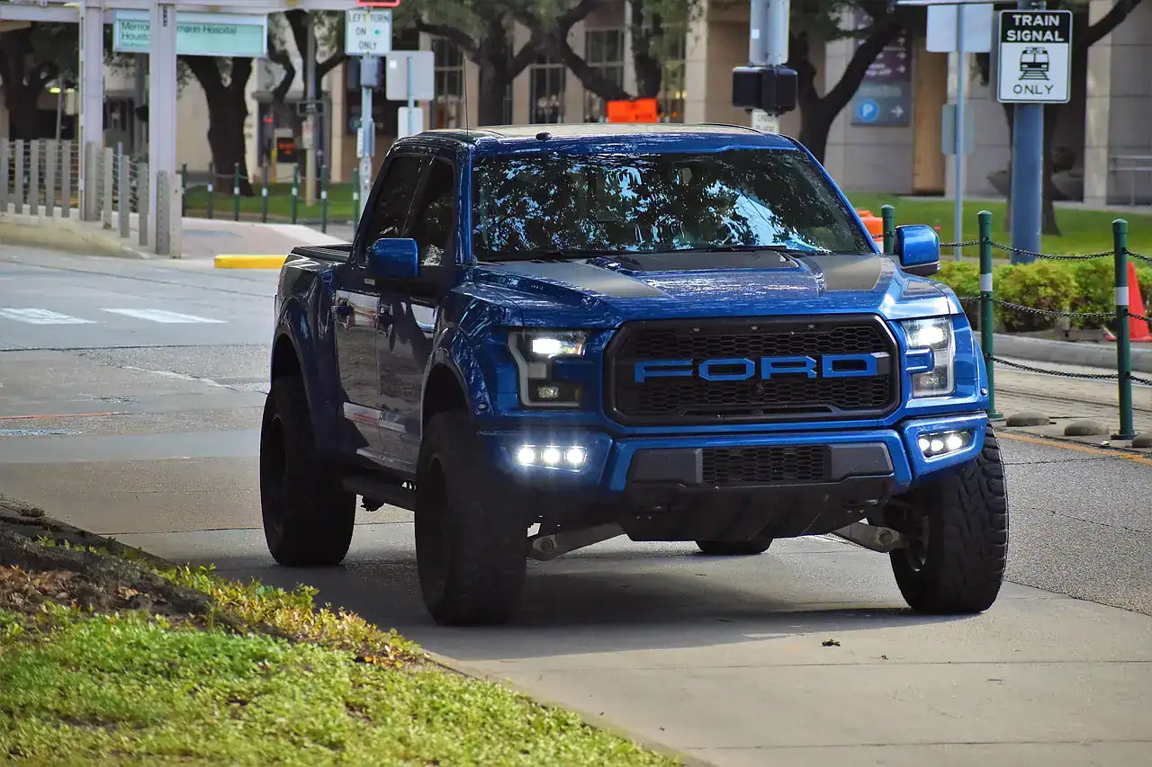 Lifted blue Ford pickup truck driving on a dry paved street