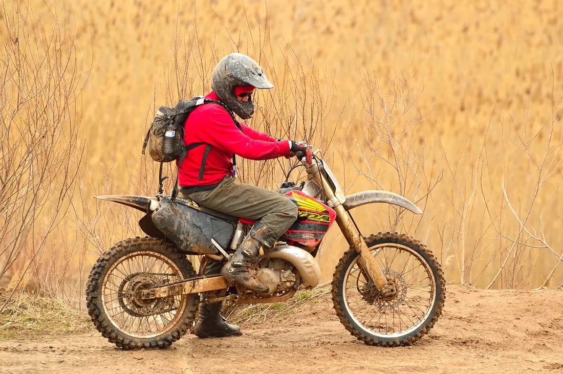 Rider on a small off-road motorcycle on a dirt trail with a backpack and helmet (not a TT-R125)