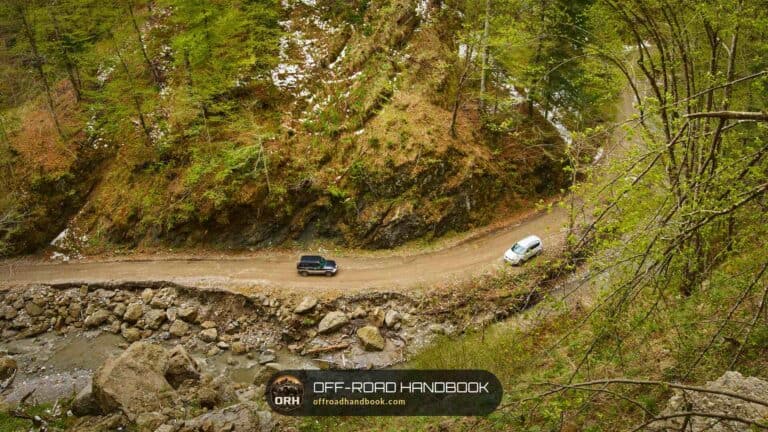 Two SUVs driving a narrow gravel road cut into a steep forested mountainside — Off-Road Handbook