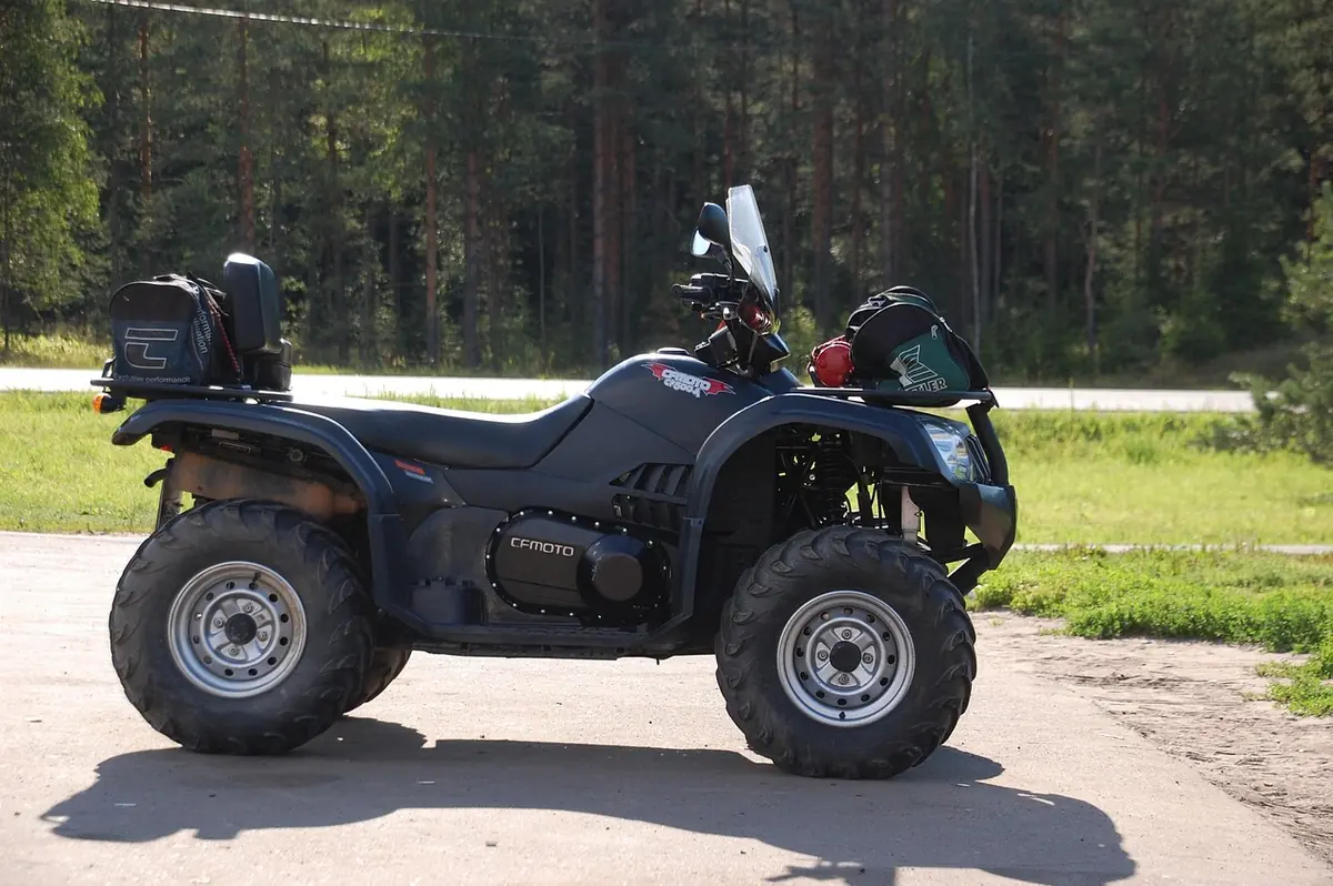 A black utility ATV with front and rear racks and a windshield parked on a gravel road (a CFMoto, not a Tracker)