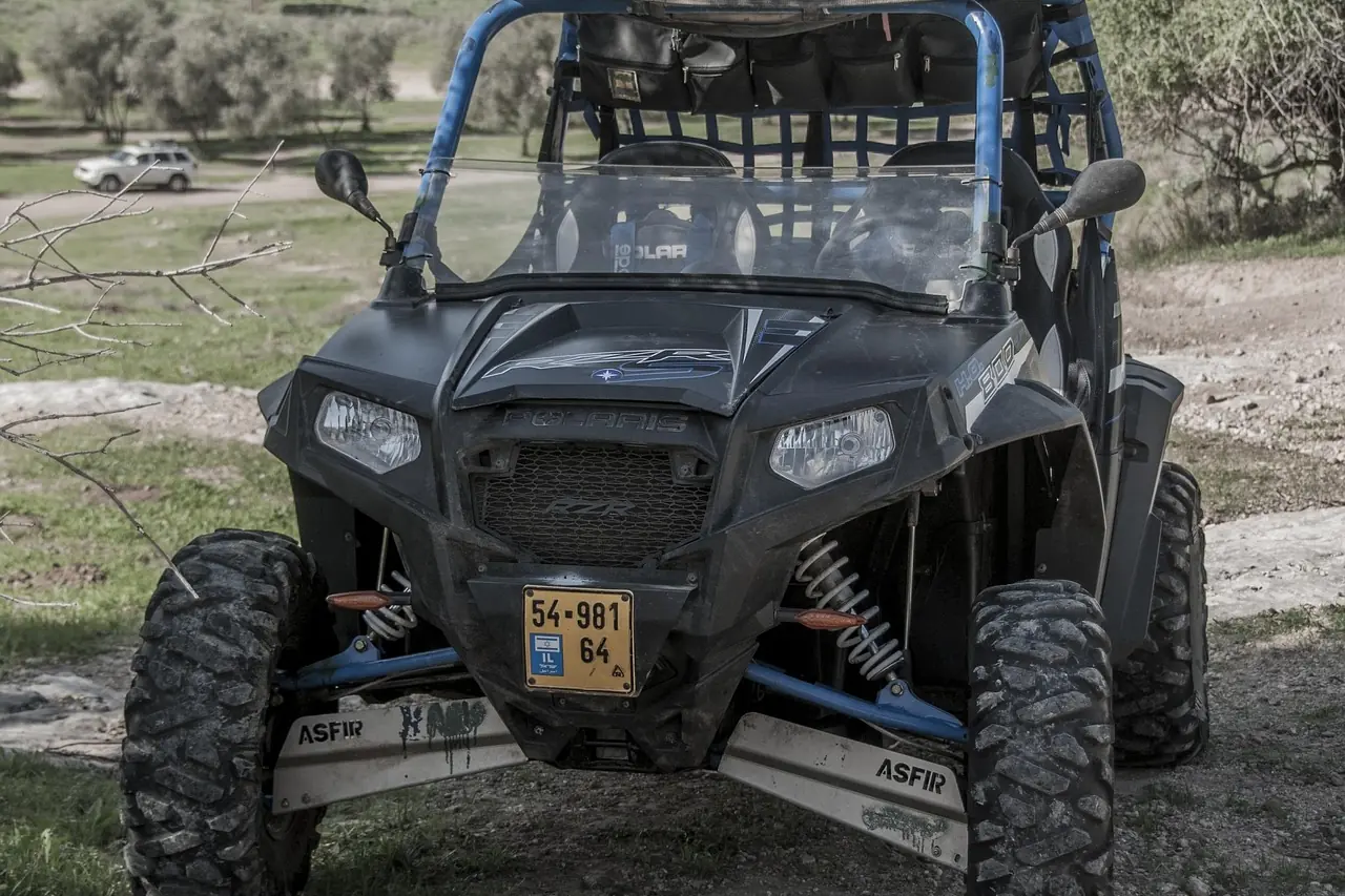 Front view of a black side-by-side UTV with knobby tires and roof stopped on a dirt trail