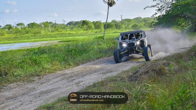 Side-by-side UTV with headlights on driving a grassy dirt trail — Off-Road Handbook