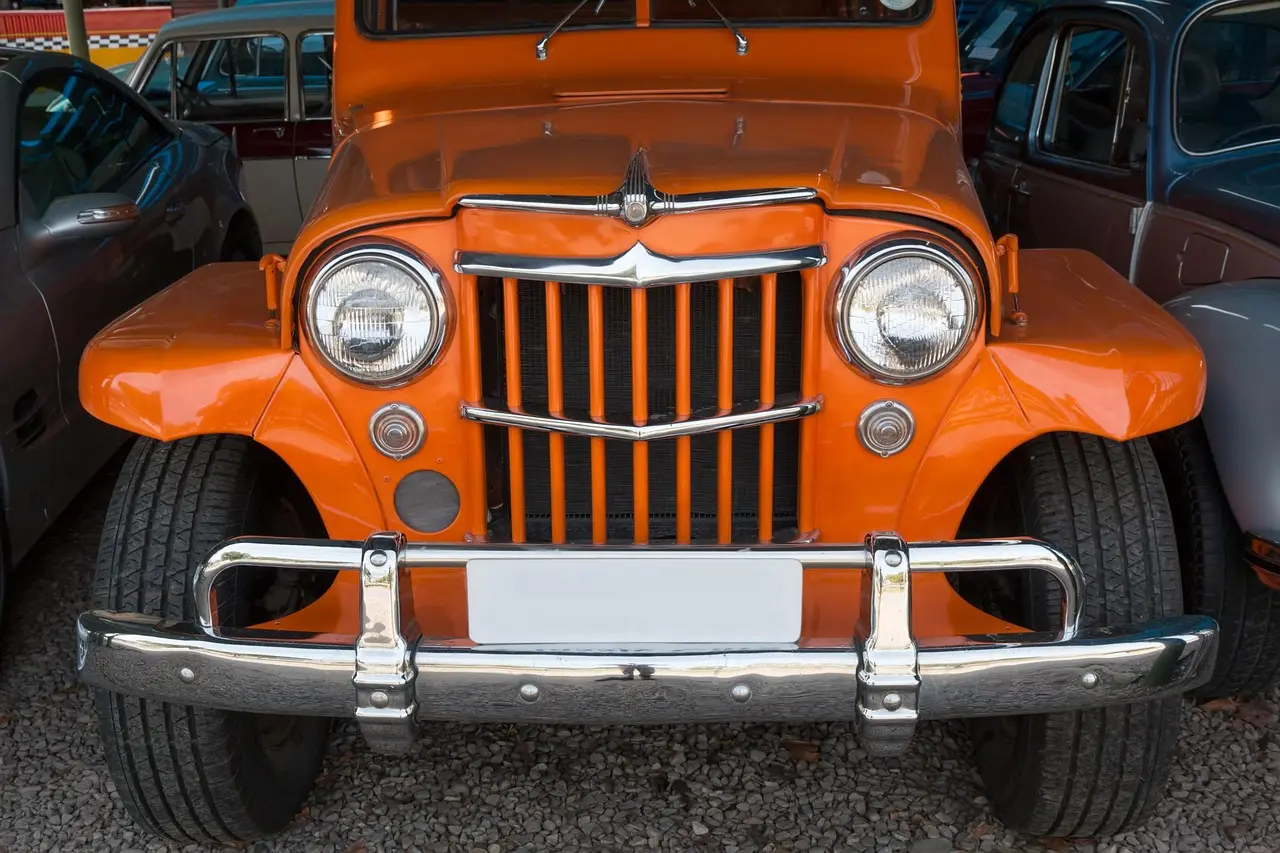 Orange vintage Willys station wagon seen from the front with a chrome vertical-slat grille, round headlights and chrome bumper