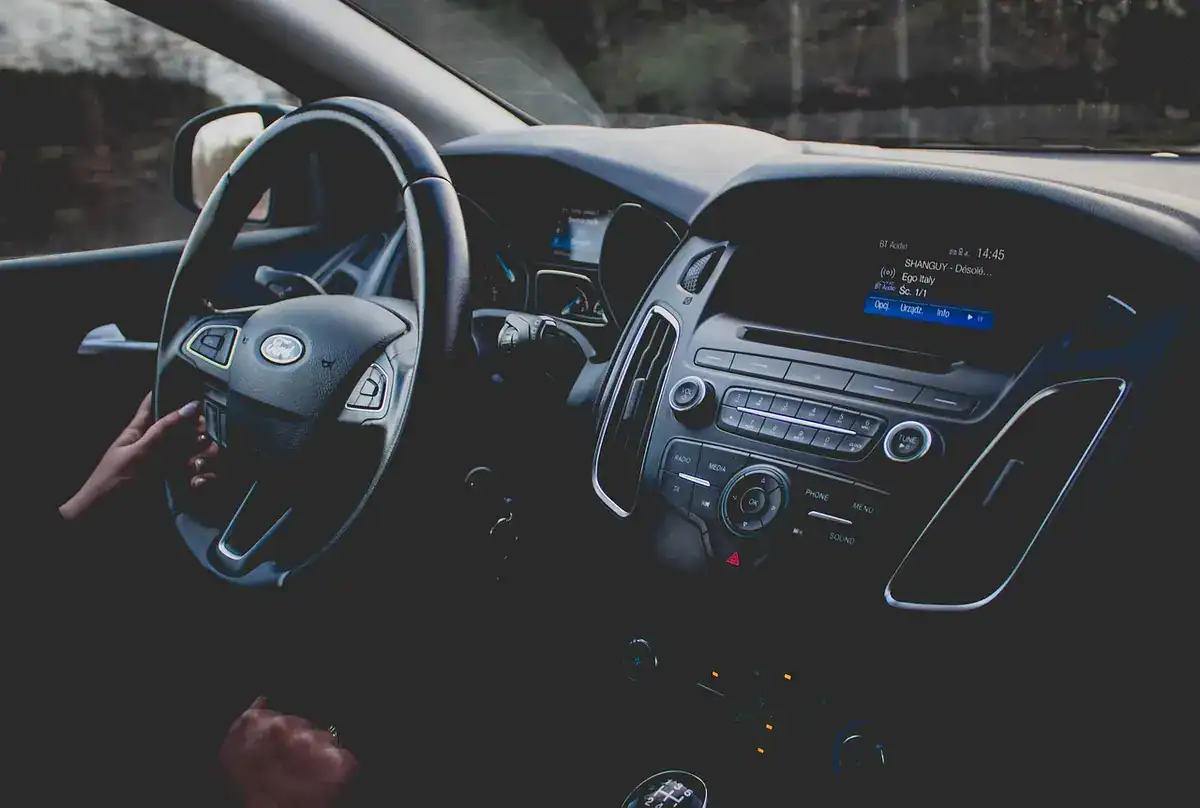 Driver’s hand on a steering wheel in a car interior with dashboard and screen