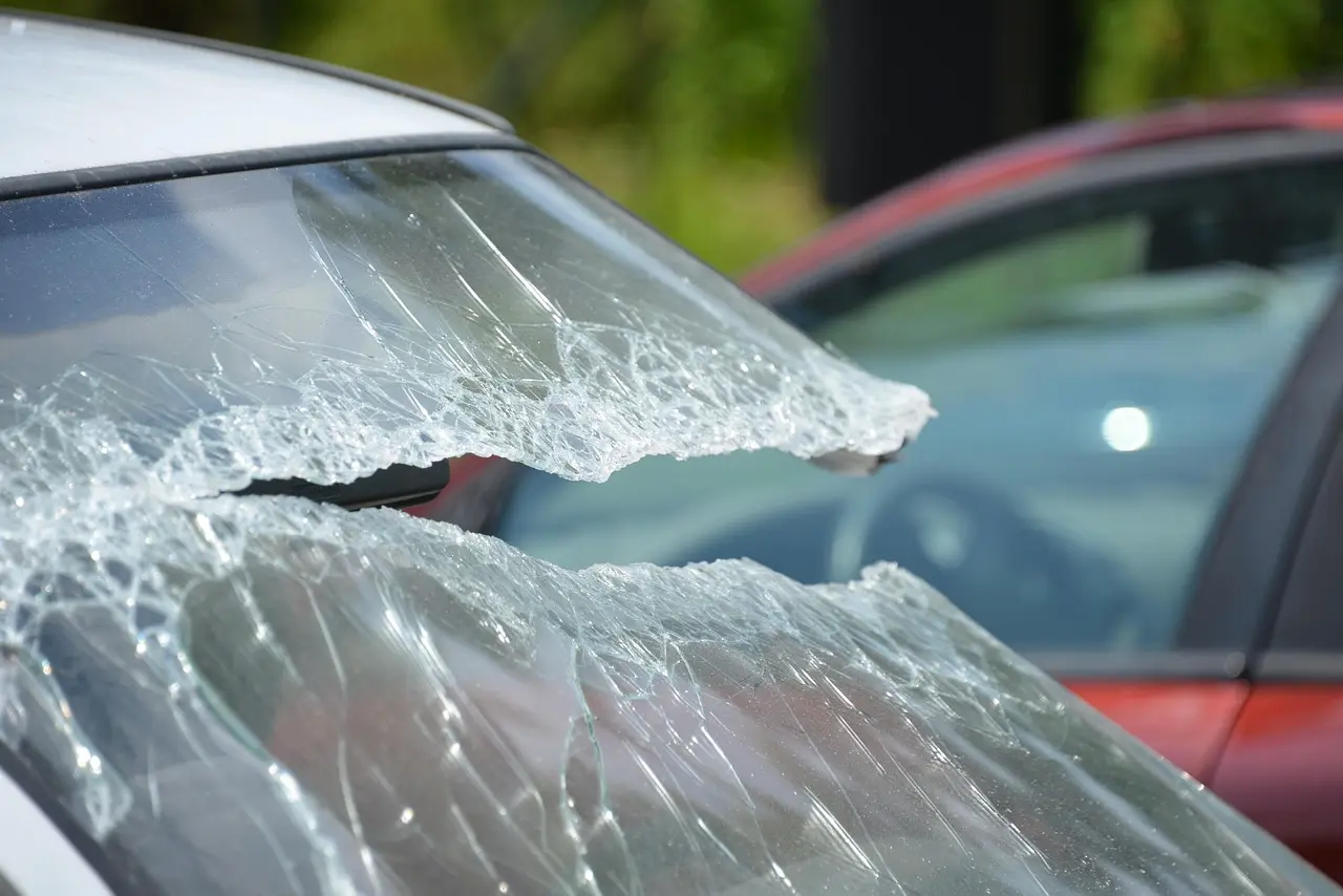 Heavily cracked windshield glass with a broken section on a parked car
