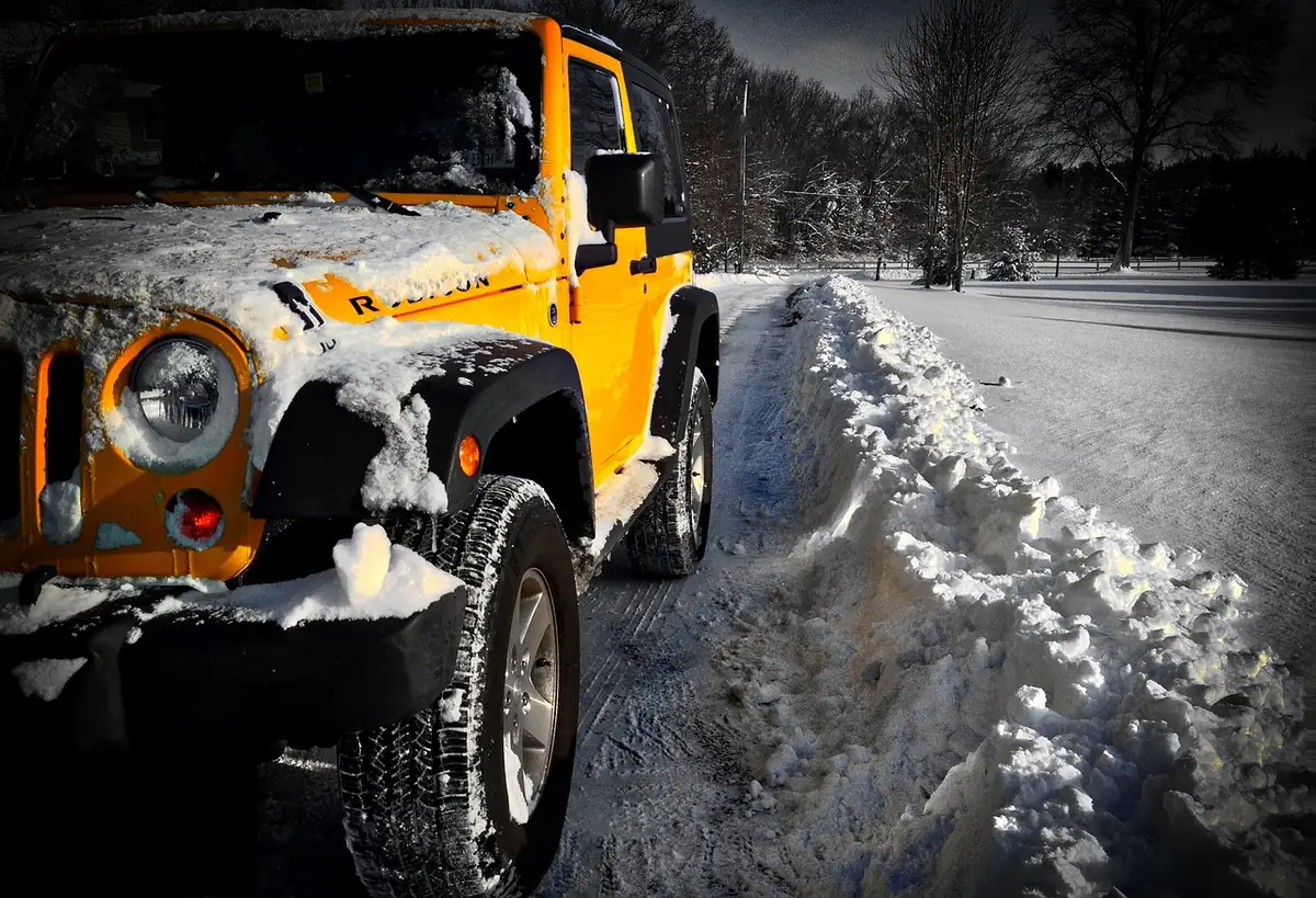 Yellow Jeep Wrangler Rubicon with snow on the hood parked beside a plowed snowbank