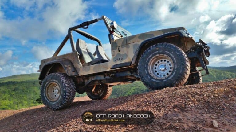 Camouflage-painted open-top Jeep with a Jeep badge climbing a red dirt hill