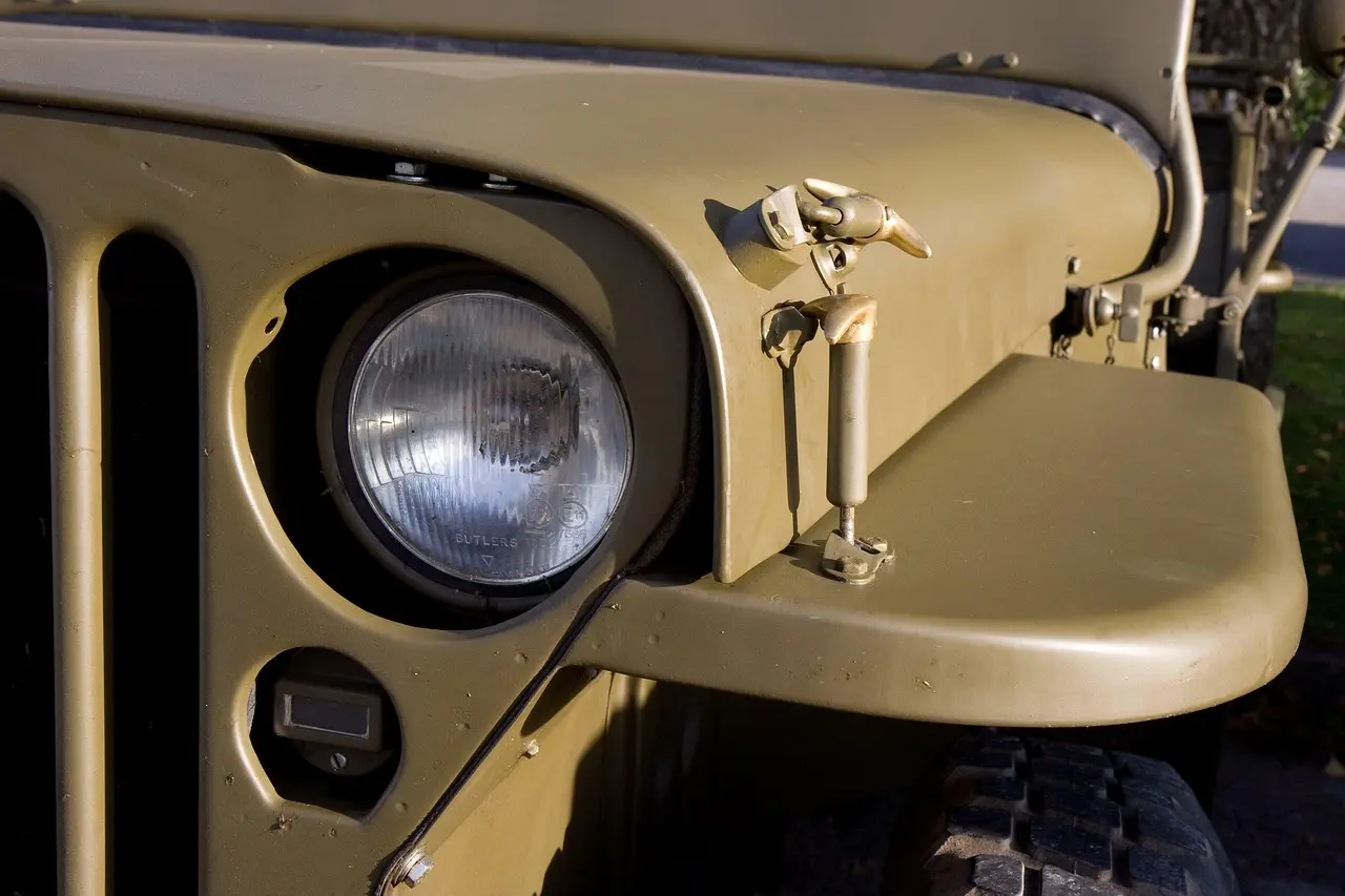 Close-up of an olive-drab military-style Jeep with a round headlight beside the vertical grille slots