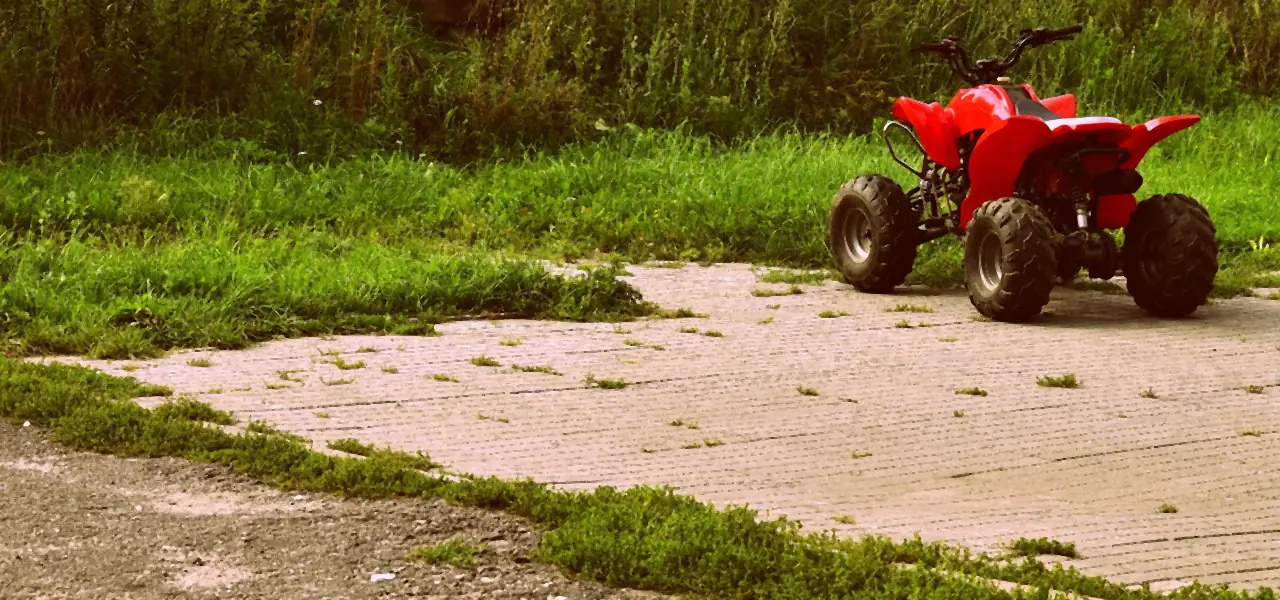 A small red youth-size ATV parked on a paved strip beside grass (not a Tracker model)