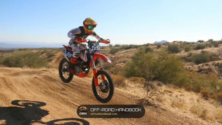 Rider on a small orange dirt bike jumping on a desert trail